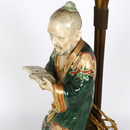 169 - A Japanese 19th century porcelain figure of a man holding a book, mounted on a gilt-metal lamp stand... 