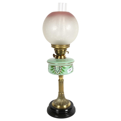 648 - A Victorian brass oil lamp, with a cranberry and clear glass etched shade and painted green glass fo... 