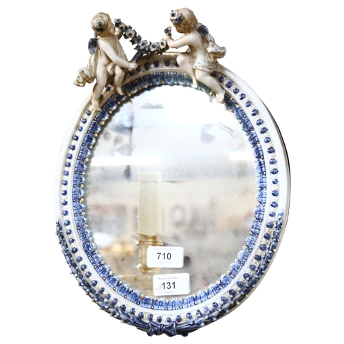 710 - A porcelain framed oval wall mirror, surmounted by angels, height 32cm