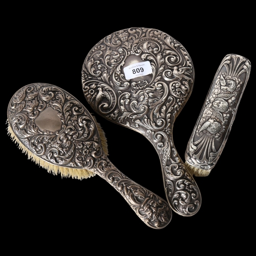 809 - An Art Nouveau silver-backed dressing table mirror and 2 brushes, with ornate scrolled and embossed ... 