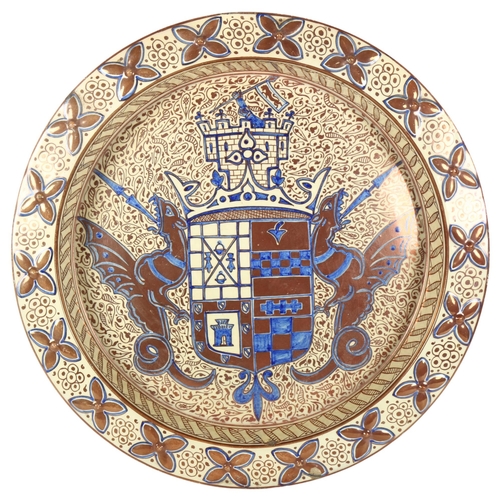 634 - A large Continental plaque with embossed copper lustre border, and a heraldic armorial, supported by... 