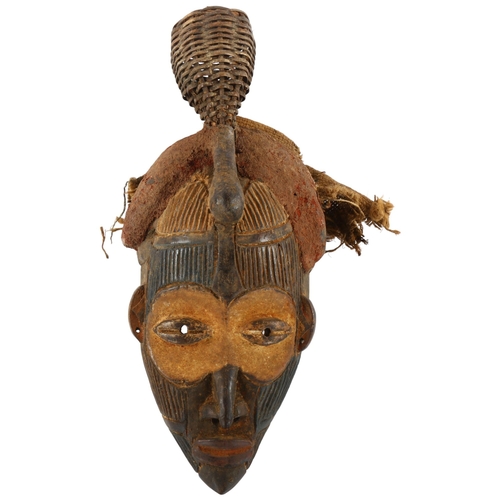 69 - An African carved wood tribal mask with basket weave rattle headdress, height 42cm