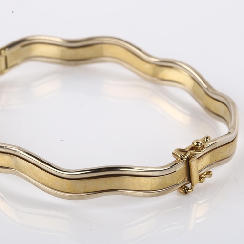 1206 - A 9ct two-tone gold hinged bangle, wave design, band width 7.7mm, internal circumference 18cm, 13.2g