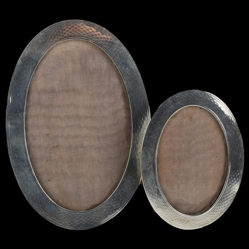 1542 - A graduate pair of Art Deco George V silver-fronted oval photo frames, with engine turned decoration... 