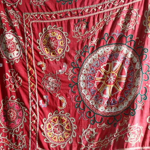 630 - A mid-20th century Uzbek Suzani with embroidered patterns on a red cloth base, 175cm x 160cm