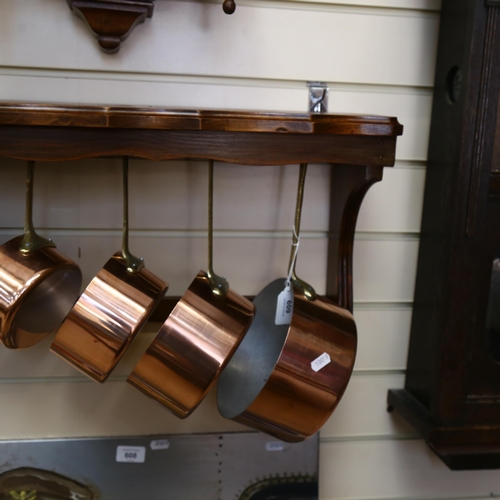 609 - A graduated set of copper and brass pans, with wall-mounted wooden hanging rack, W56cm