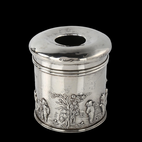 1596 - An Edwardian silver dressing table hair tidy box, cylindrical form with relief embossed country land... 