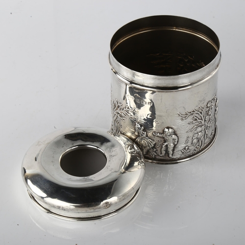 1596 - An Edwardian silver dressing table hair tidy box, cylindrical form with relief embossed country land... 