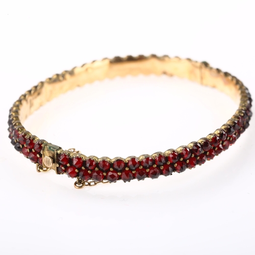 1350 - A Victorian double-row garnet hinged bangle, unmarked yellow metal closed-back settings with faceted... 