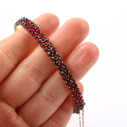 1350 - A Victorian double-row garnet hinged bangle, unmarked yellow metal closed-back settings with faceted... 