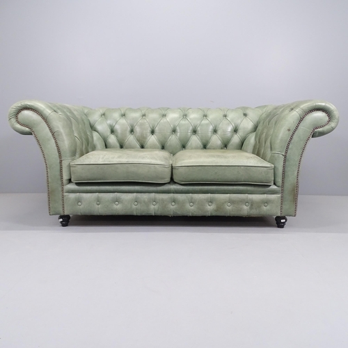 2193 - A green button back leather upholstered Chesterfield sofa with rollover arms, and raised on turned l... 