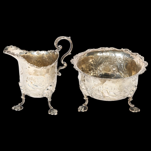 1040 - An ornate Victorian silver cream jug, with allover relief embossed and engraved decoration, on cast ... 