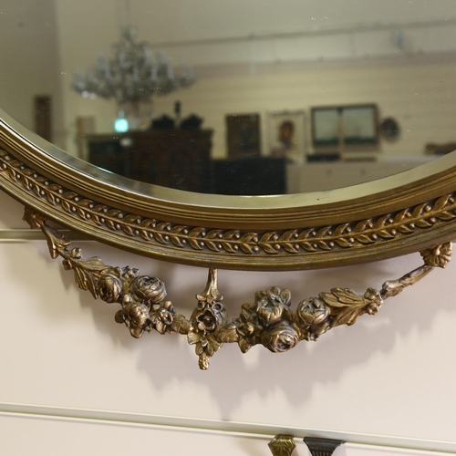 71 - An oval gilt-gesso framed wall mirror, with ribbon pediment, circa 1920, width excluding ribbons 87c... 