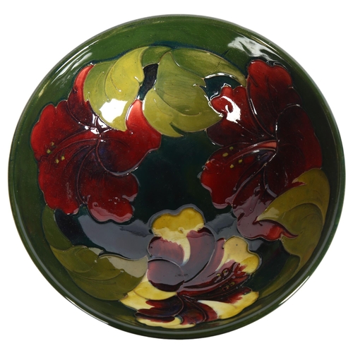 1011 - A Moorcroft green ground bowl on foot, with tube-lined Hibiscus design, with paper label, 15.5cm