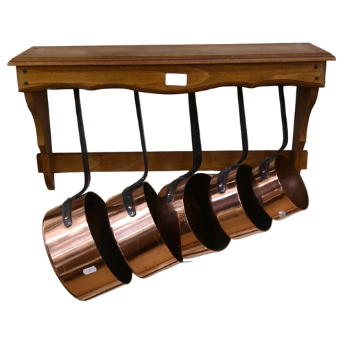 1054 - A graduated set of French copper and steel-handles pans, with hanging rack, width 58cm