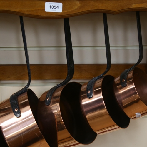 1054 - A graduated set of French copper and steel-handles pans, with hanging rack, width 58cm