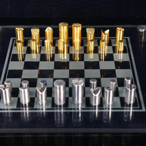 514 - A Modernist hand turned steel and brass chess set, with glass chess board in original leather case, ... 