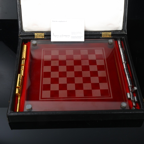 514 - A Modernist hand turned steel and brass chess set, with glass chess board in original leather case, ... 