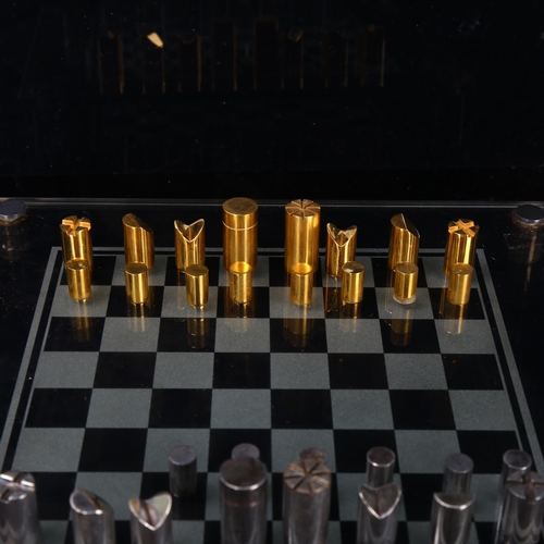 515 - A Modernist hand turned steel and brass chess set, with glass chess board in original leather case, ... 