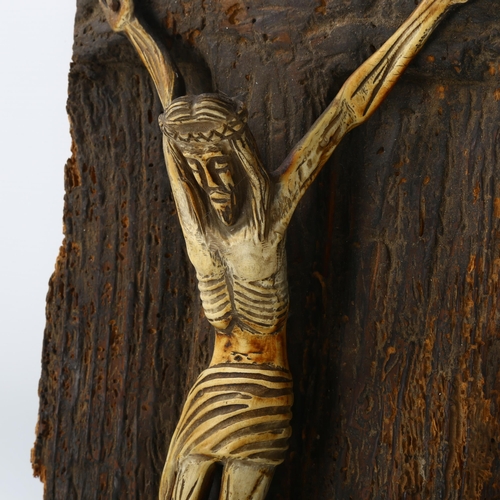 193 - A naive carved bone crucifix mounted on rustic wooden ground, length 42cm