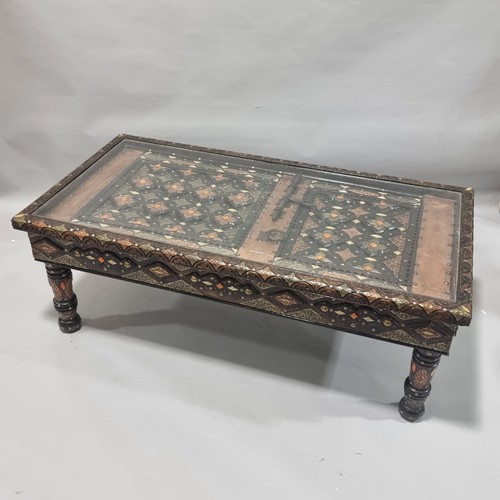 263 - An ornate Moroccan centre table, made from an Antique studded and metal inlaid door behind a glass p... 