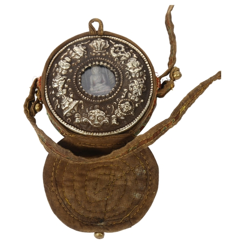 409 - A Tibetan white metal travelling gau box of circular form, the front embossed with Buddhist emblems,... 