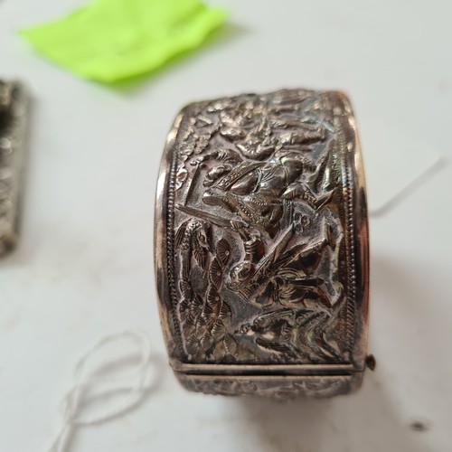 1013 - A Chinese embossed silver hinged bangle, panels decorated with hunting figures, with maker's mark fo... 