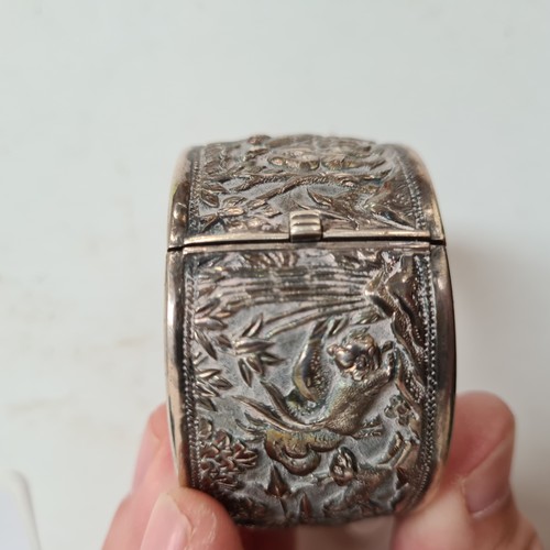 1013 - A Chinese embossed silver hinged bangle, panels decorated with hunting figures, with maker's mark fo... 