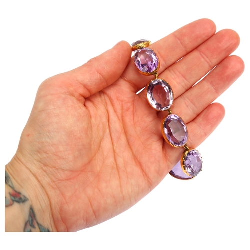 1104 - A Victorian amethyst Riviere necklace, the graduated oval amethysts set in unmarked gold cut-down co... 