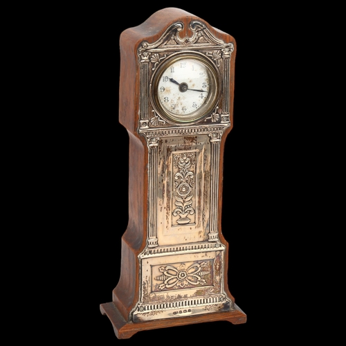 1434 - A silver-fronted mantel clock in the form of a longcase clock, with embossed mounts and enamel dial,... 