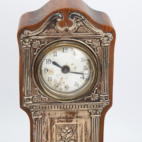 1434 - A silver-fronted mantel clock in the form of a longcase clock, with embossed mounts and enamel dial,... 