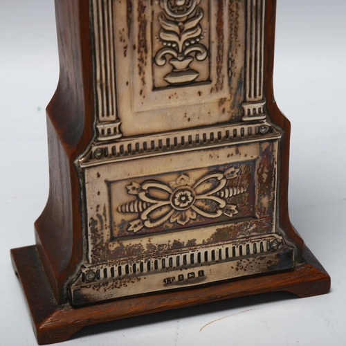 1434 - A silver-fronted mantel clock in the form of a longcase clock, with embossed mounts and enamel dial,... 