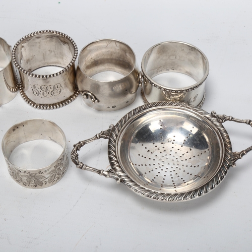 1444 - A group of various silver napkin rings, a George III silver caddy spoon, and a plated tea strainer o... 