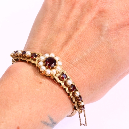 1131 - A mid-20th century 9ct gold garnet and pearl cluster hinge bangle, with central flowerhead cluster f... 