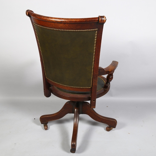 25 - An early 20th century oak revolving office elbow chair, with buttoned green leather upholstery