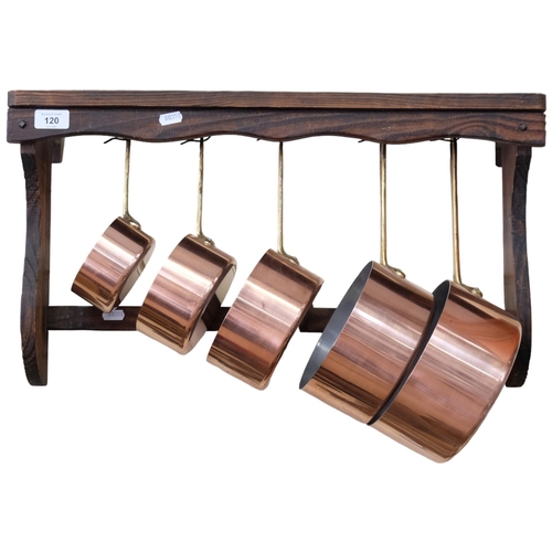 120 - A graduated set of 5 copper bound and brass-handled pans, complete with an oak hanging rack