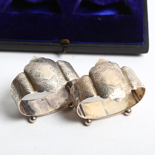 1298 - A pair of Edward VII engraved silver napkin rings, standing on ball feet, in fitted box, retailed by... 