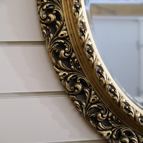 814 - A large wooden oval wall-hanging bevel-edge mirror, in ornate giltwood frame, 76cm x 63cm