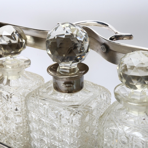 290 - A plated 3-bottle tantalus, circa 1900, containing 3 square cut-glass decanters, 1 with hallmarked s... 