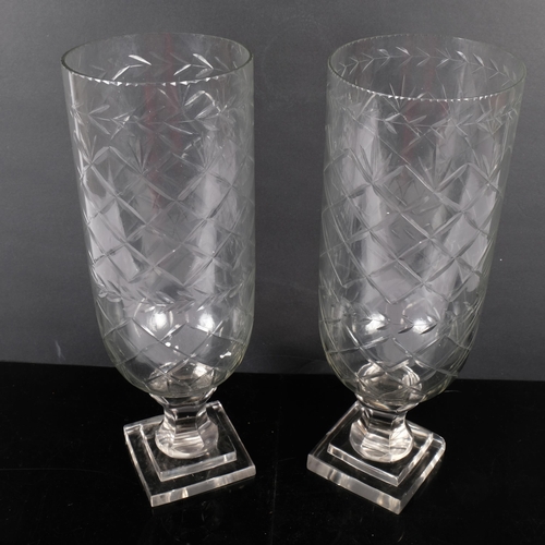 143 - A pair of cut glass hurricane lanterns on square plinths. H - 34cm.