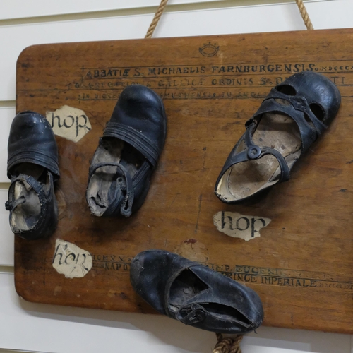 619 - A folk art sculpture - group of 5 antique children's shoes, mounted on board, with roman script. W -... 