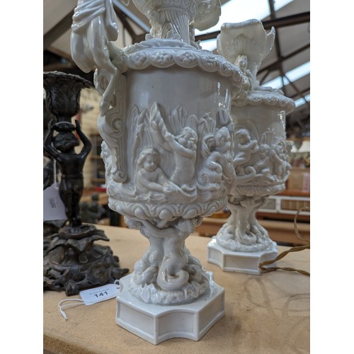 141 - A pair of continental ceramic ewers with embossed figural an cherub decoration. Both marked to under... 