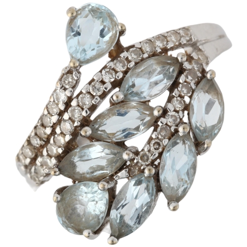 1129 - A modern 9ct white gold blue topaz and diamond crossover ring, maker KRM, London 2008, floral motif ... 