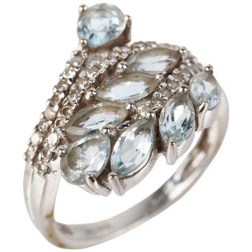 1129 - A modern 9ct white gold blue topaz and diamond crossover ring, maker KRM, London 2008, floral motif ... 