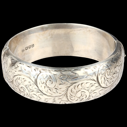 1372 - A mid-20th century silver hinged bangle, maker S&E, Chester 1954, allover engraved foliate decoratio... 