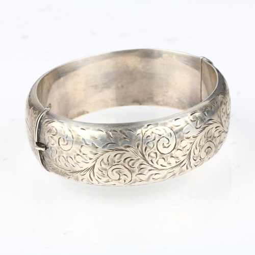 1372 - A mid-20th century silver hinged bangle, maker S&E, Chester 1954, allover engraved foliate decoratio... 