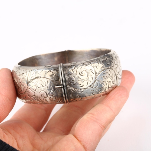 1372 - A mid-20th century silver hinged bangle, maker S&E, Chester 1954, allover engraved foliate decoratio... 