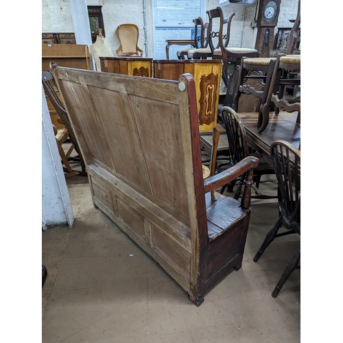 2184 - An antique stained pine settle, with panelled back and lifting seats. Overall 129x118x55cm, seat 116... 