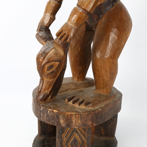 81 - An early/mid 20th century Cameroon carving, of a chief on a stool with a bats head mask, height 65cm