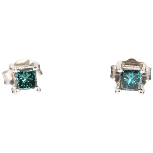 1129 - A pair of solitaire blue diamond earrings, claw set with Princess-cut diamonds with stud fittings, a... 